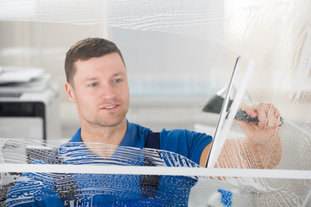 Worker Cleaning Soap Sud On Window With Squeegee